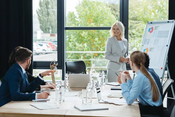 Smiling Businesswoman Standing Flipchart Business Meeting Young Colleagues — Stock Photo, Image