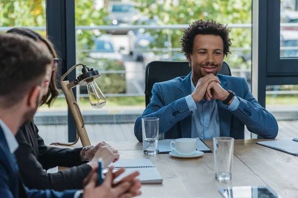 Sorridente Empresário Afro Americano Sentado Mesa Perto Colegas Sala Reuniões — Fotografia de Stock