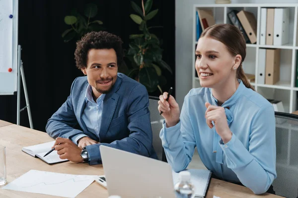 Fröhliche Geschäftsfrau Sitzt Neben Einem Afrikanisch Amerikanischen Kollegen Und Zeigt — Stockfoto