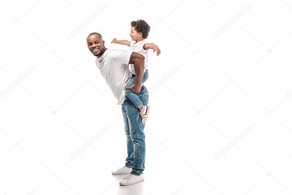 cheerful african american man piggybacking adorable son and smiling at camera on white background