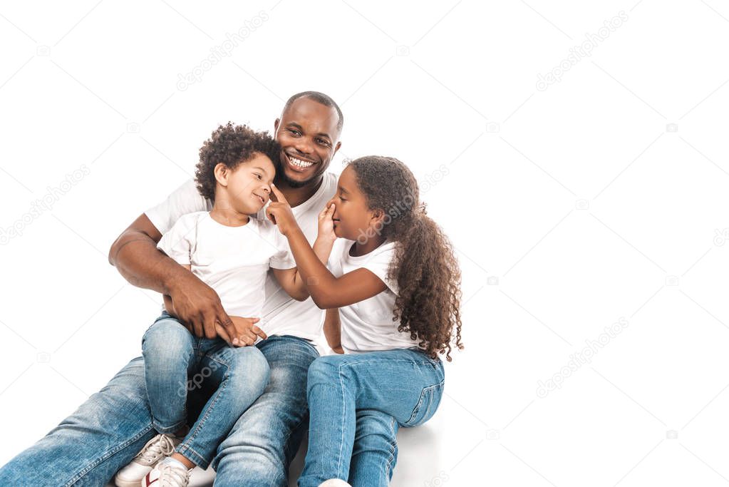 cheerful african american brother and sister touching noses of each other while sitting with dad on white background