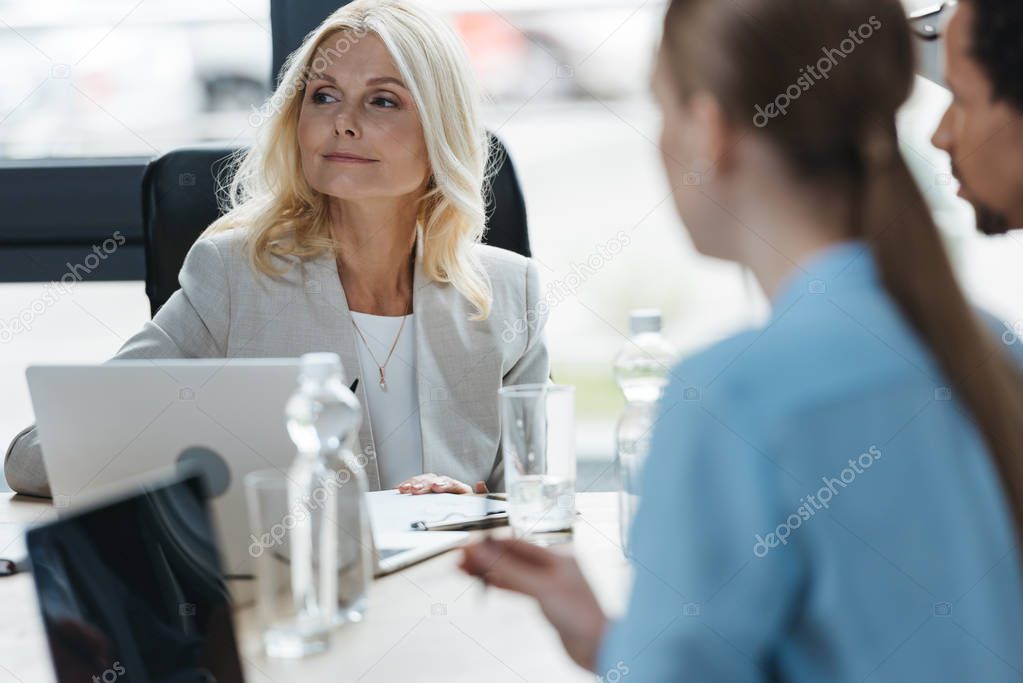 selective focus of confident businesswoman at business meeting with young multicultural colleagues