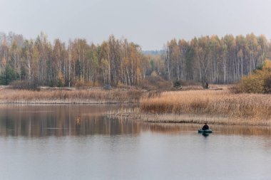 LVIV, UKRAINE - 23 Ekim 2019: balıkçının teknede oturup gölde balık tutarken olta tutuşu