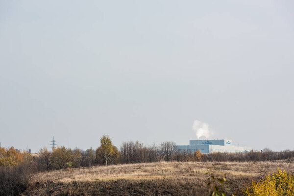LVIV, UKRAINE - OCTOBER 23, 2019: smoke near factory with cersanit lettering and green trees against sky 