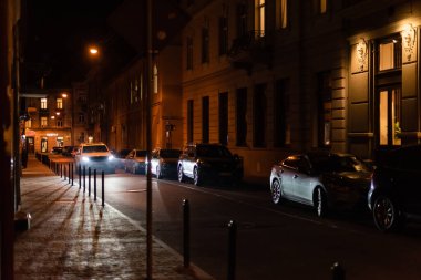 LVIV, UKRAINE - OCTOBER 23, 2019: lighting from car on street near buildings with cyrillic lettering at night  clipart