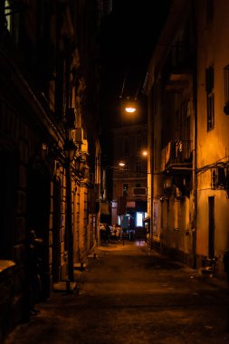 Karanlık sokakta eski evlerle yürüyen insanlar. 