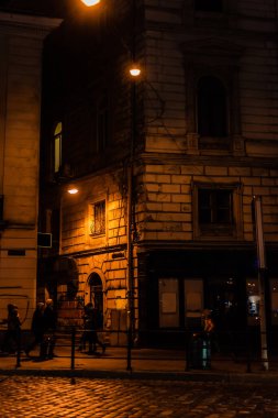 LVIV, UKRAINE - 23 Ekim 2019: Karanlık sokaktaki insanların yakınında sokak lambaları 