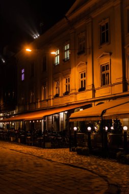 dark street and silhouette of people sitting in cafe with terrace  clipart