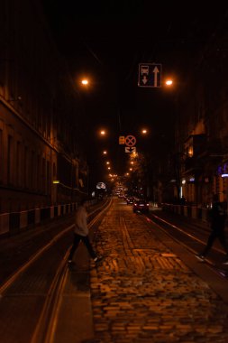 LVIV, UKRAINE - OCTOBER 23, 2019: silhouette of people crossing road near cars at night clipart