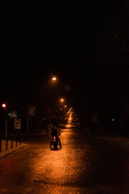 LVIV, UKRAINE - 23 Ekim 2019: gece sokakta scooter süren kasklı bir adamın silueti 