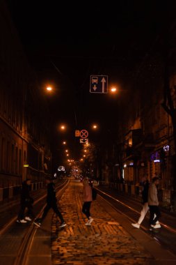 LVIV, UKRAINE - OCTOBER 23, 2019: silhouette of people crossing road near cars in evening  clipart