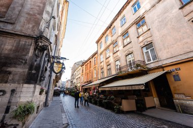 LVIV, UKRAINE - 23 Ekim 2019: İnsanlar eski evlerinde Kiril harfleriyle sokak kafesi ve tabela boyunca yürüyorlar 