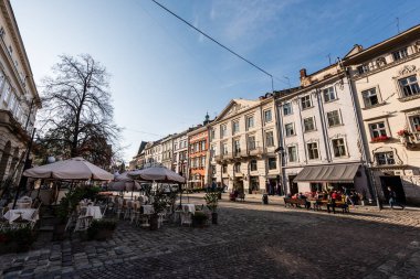 LVIV, UKRAINE - 23 Ekim 2019: insanlar şehir merkezindeki eski evlerin yakınındaki sokak kafesinde oturuyorlar