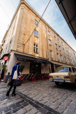 LVIV, UKRAINE - 23 Ekim 2019: Çadırda harflerle birlikte eski model araba ve kafe yakınlarında yürüyen kadın
