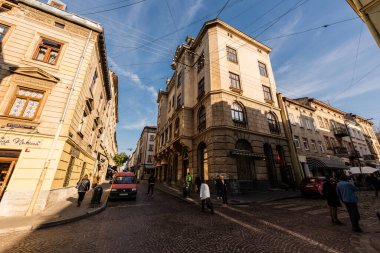 LVIV, UKRAINE - OCTOBER 23, 2019: old house with cyrillic lettering and people walking along street in city center clipart