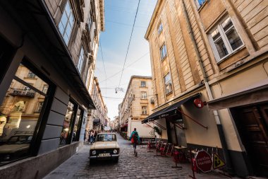 LVIV, UKRAINE - OCTOBER 23, 2019: vintage car on narrow street near cafe with lettering on tent clipart