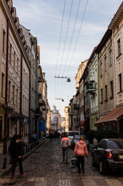 LVIV, UKRAINE - 23 Ekim 2019: park edilmiş arabalar ve levhada Kiril harfleriyle evin yakınında yürüyen insanlar 