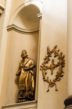 LVIV, UKRAINE - OCTOBER 23, 2019: gilded statue of priest near cross in wreath in dominican church clipart