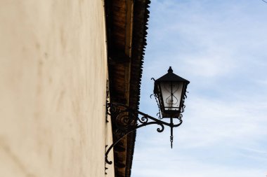low angle view of vintage lantern made of forged iron on stone wall against blue sky in lviv, ukraine clipart