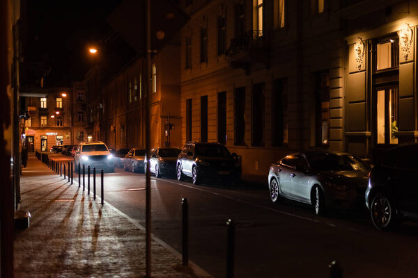 LVIV, UKRAINE - OCTOBER 23, 2019: lighting from car on street near buildings with cyrillic lettering at night 