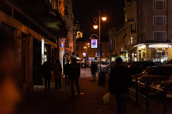 Львов, Украина - 23 октября 2019 года: люди идут по темной улице рядом со зданием Макдональдса
 