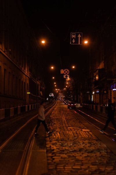 LVIV, UKRAINE - OCTOBER 23, 2019: silhouette of people crossing road near cars at night