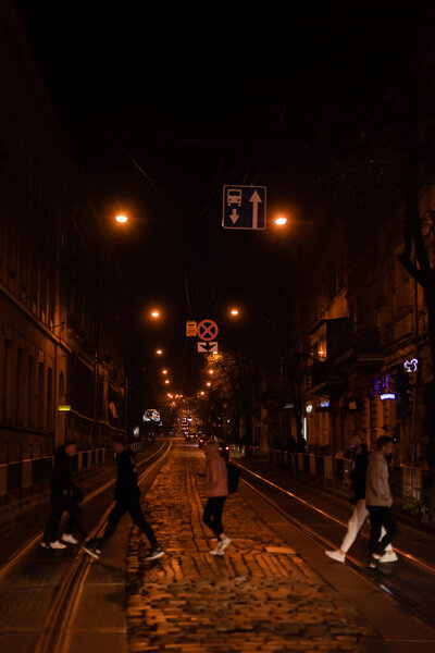 LVIV, UKRAINE - OCTOBER 23, 2019: silhouette of people crossing road near cars in evening 