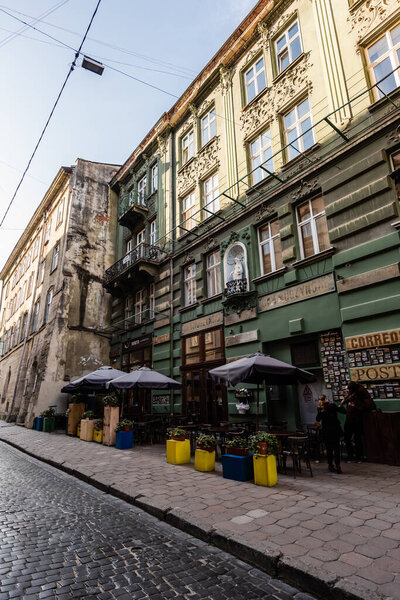 LVIV, UKRAINE - OCTOBER 23, 2019: street cafe with plants in flowerpots near old house with latin lettering 