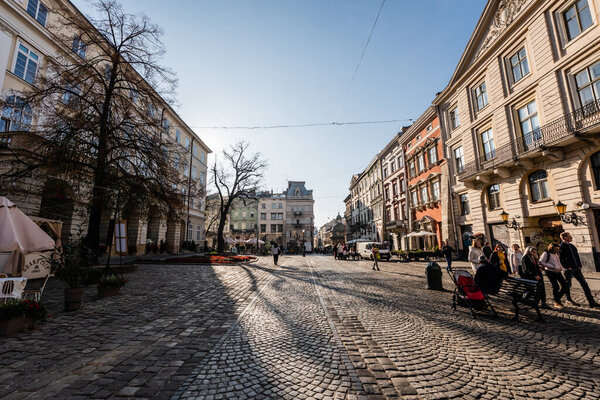 LVIV, UKRAINE - OCTOBER 23, 2019: old buildings and people walking along cafe with grand cafe leopolis lettering on signboard