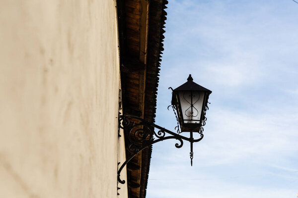 low angle view of vintage lantern made of forged iron on stone wall against blue sky in lviv, ukraine