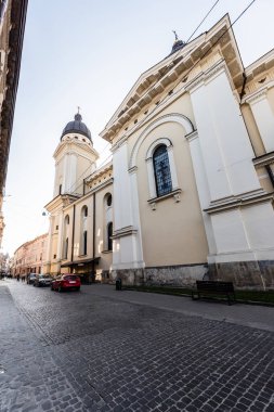LVIV, UKRAINE - OCTOBER 23, 2019: carmelite monastery wall and church, and cars parked on street clipart