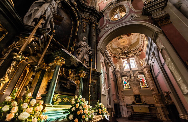 LVIV, UKRAINE - OCTOBER 23, 2019: low angle view of carmelite church interior decorated with gilding, sculptures and natural flowers