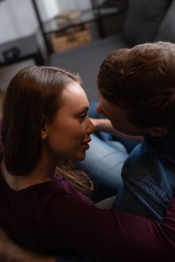 Çekici bir kadın ve sarılı bir adam oturma odasında birbirlerine bakıyorlar. 