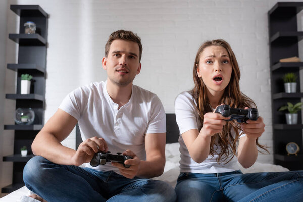 KYIV, UKRAINE - MAY 15, 2020: surprised woman and emotional man playing video game in bedroom 