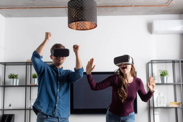 リビングルームでゲームをしながら勝利を祝う仮想現実ヘッドセットで幸せなカップル — ストック写真