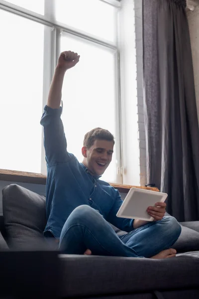 Podekscytowany Mężczyzna Ręką Nad Głową Patrząc Cyfrowy Tablet Salonie — Zdjęcie stockowe