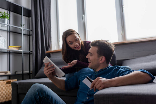 cheerful woman looking at man holding credit card near digital tablet 