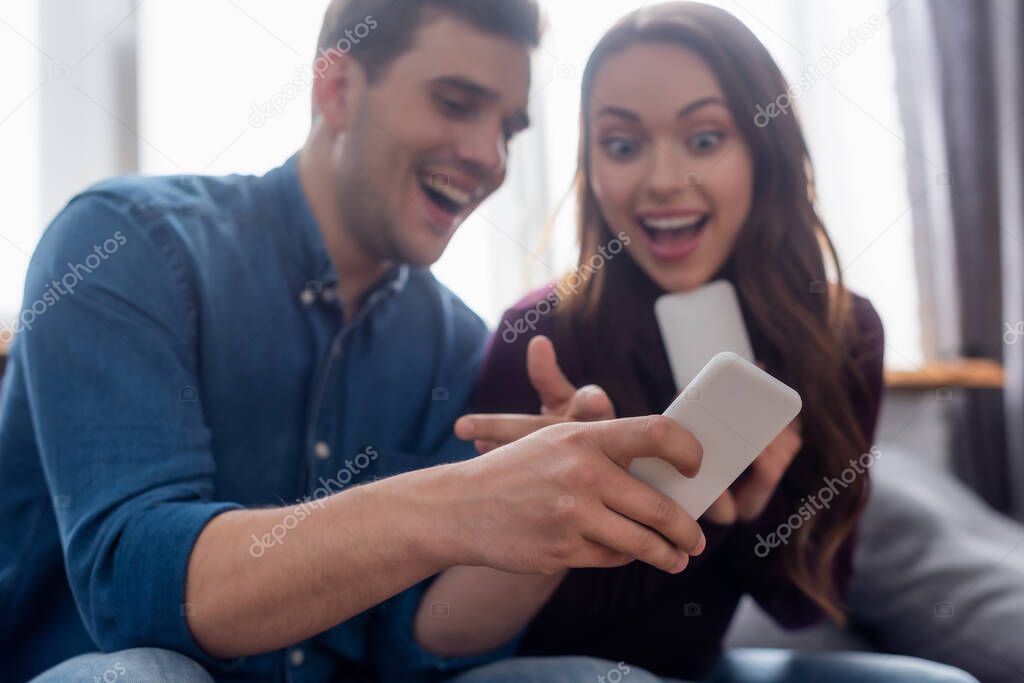 selective focus of cheerful man pointing with finger at smartphone near excited girl 