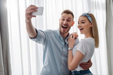 Heyecanlı bir adamın neşeli bir kızla selfie çektiği seçici odak noktası. 