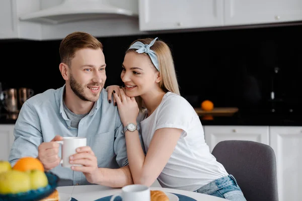 キッチンでコーヒーを飲みながら幸せなボーイフレンドに触れる女の子の選択的な焦点 — ストック写真