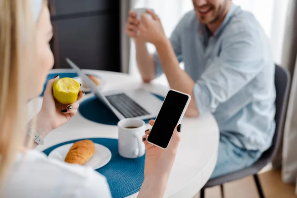 带着空白屏幕的智能手机和苹果的女性 接近快乐的自由职业者和早餐的选择性焦点 — 图库照片