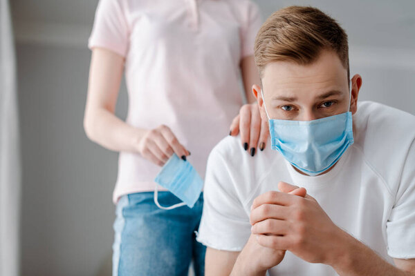 selective focus of woman touching man in medical mask at home 