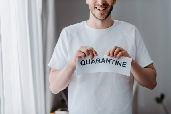 cropped view of happy man ripping paper with quarantine lettering 