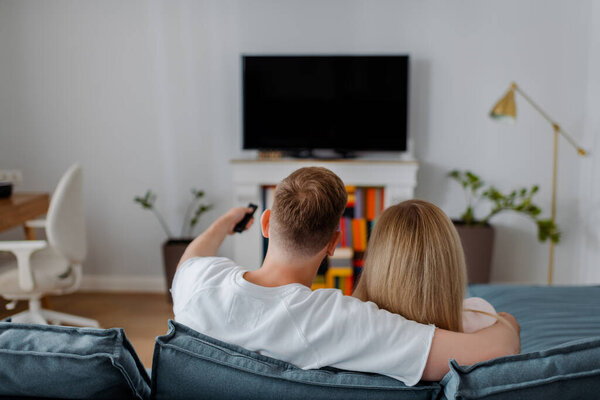 back view of man and woman sitting near flat panel tv with blank screen