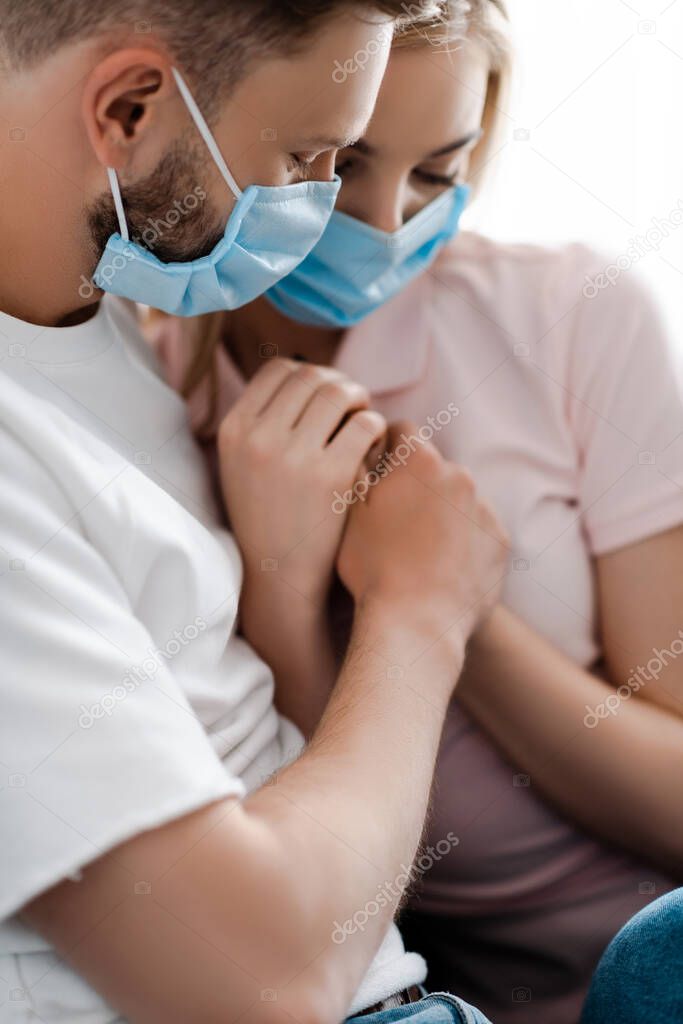 selective focus of couple in medical masks holding hands