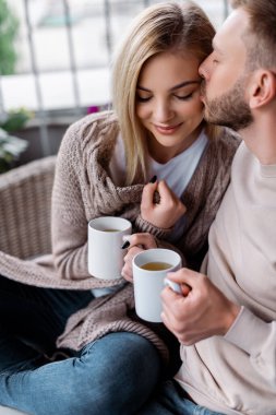 Seçici odak noktası, bir fincan çayla mutlu bir kadının yanağını öpmek.