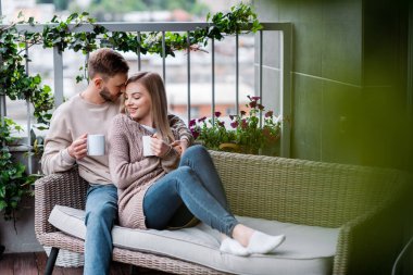 Seçici odak noktası mutlu adam ve neşeli kadın elinde çay fincanları ve açık kanepede oturuyor. 