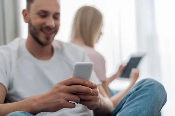 快乐男人在接近拿着数码平板电脑的女人时使用智能手机的选择性焦点 — 图库照片