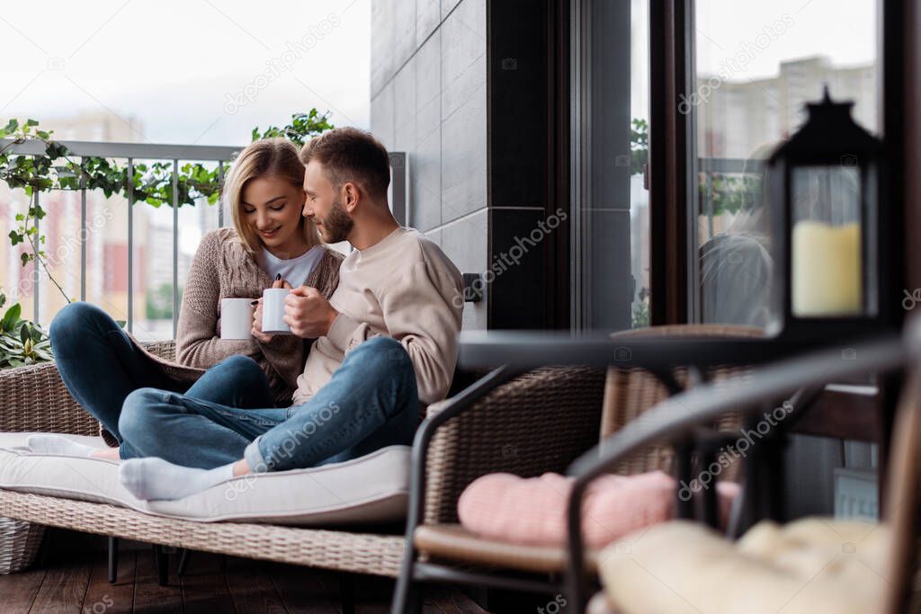 selective focus of happy woman and man holding cups while sitting on outdoor sofa