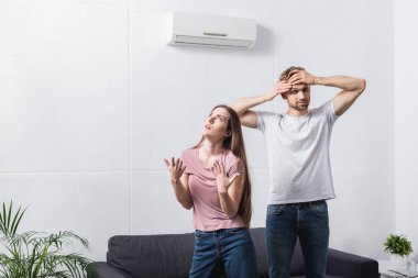 young exhausted couple suffering from heat at home with broken air conditioner  clipart